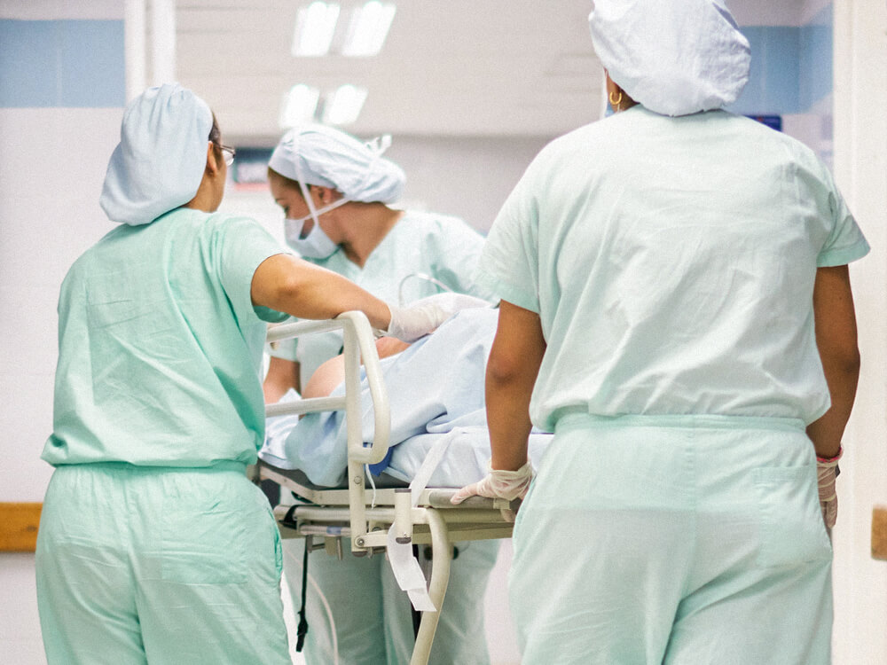 Three nurses wheel a patient in a bed through the halls of a hospital.