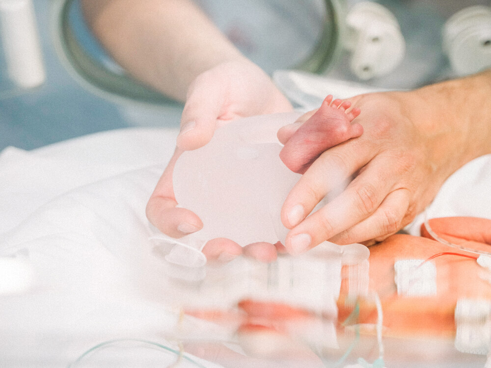 A nurse’s hands reach into an incubator and hold a newborn’s foot.