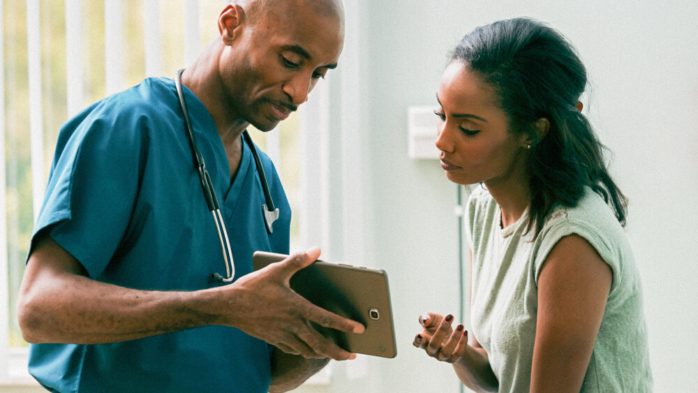 A nurse and patient look together at a tablet in a doctor’s office.