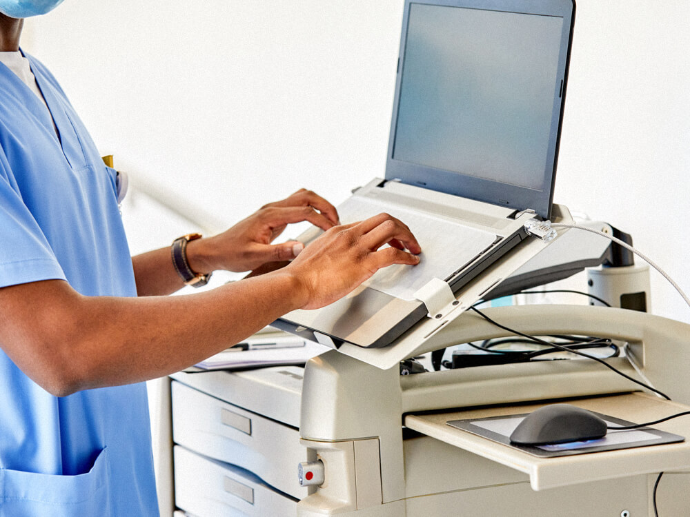 A medical professional in scrubs enters data into a computer.