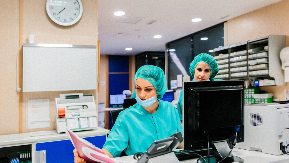 Two nurses review documents and enter information into a computer in a hospital.