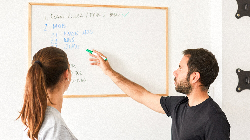 Personal trainer reviews workout written on a whiteboard with a client.