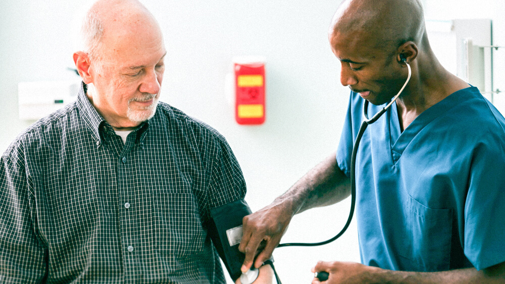 A nurse practitioner takes the blood pressure and listens to the blood flow of a senior patient.