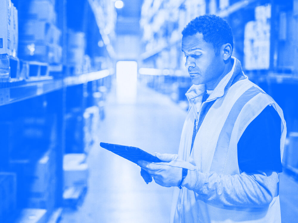 A person holds a tablet in the aisle of a warehouse.