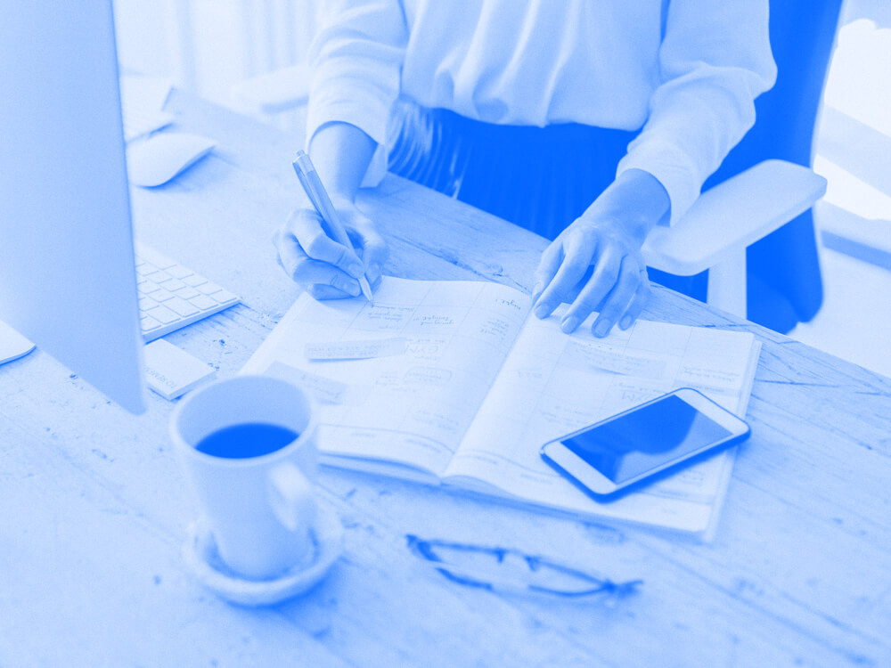 A person at their desk taking notes in a notebook.