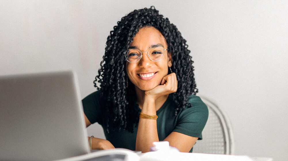 Social worker smiles at the camera while sitting at a desk with books and a laptop.