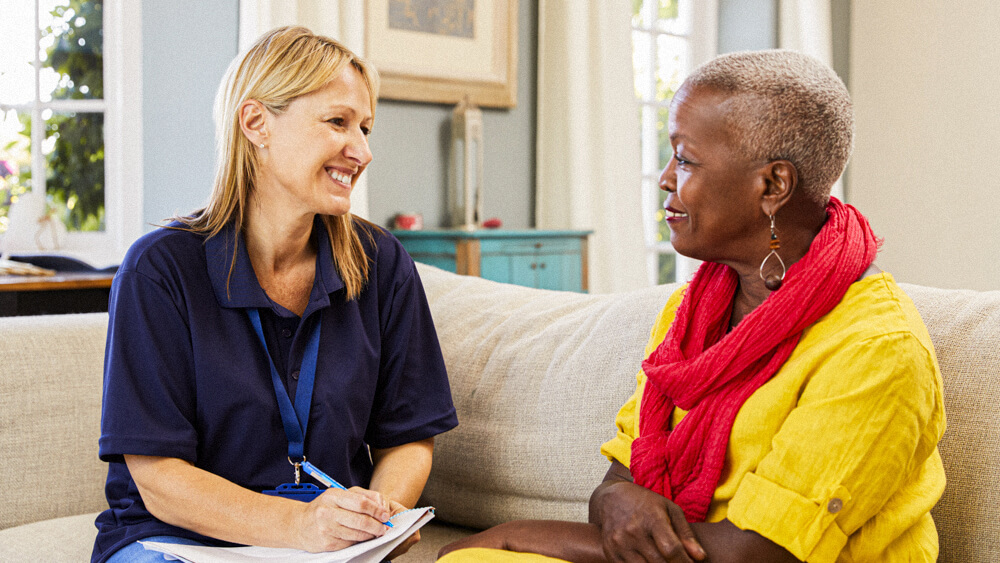 Social worker sits on a couch with an older client and takes notes.