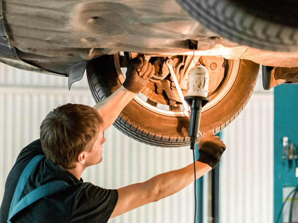 Automotive mechanic tightens a screw on a lifted vehicle.