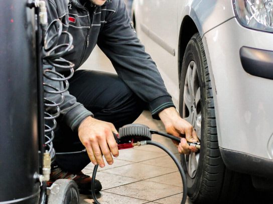 Automotive mechanic adding air in a tire.