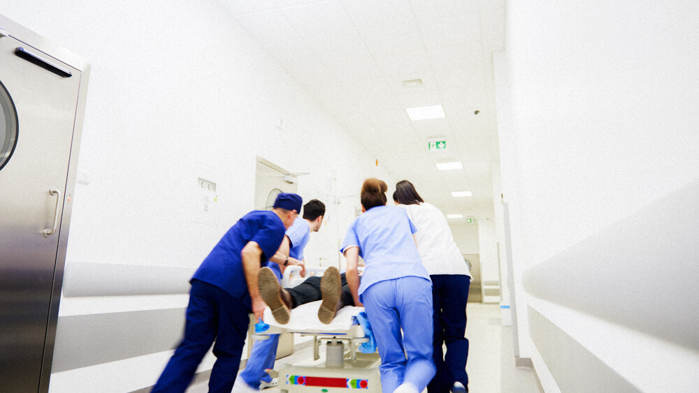 A team of nurses and medical professionals rush a patient down a hospital hall.