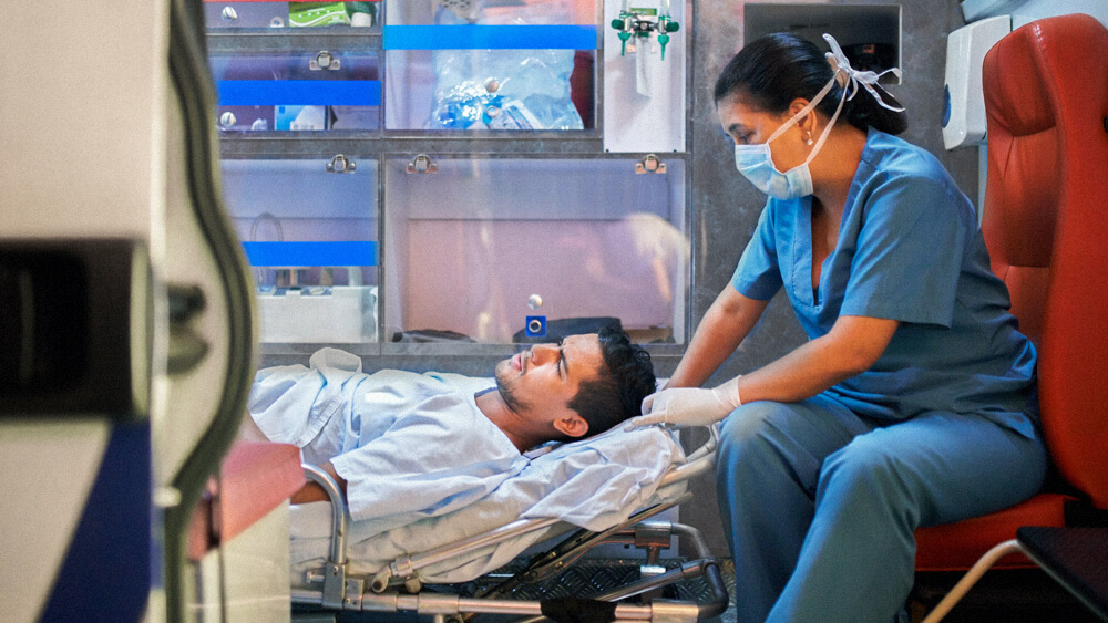 A transport nurse sits with and monitors a patient inside an ambulance.