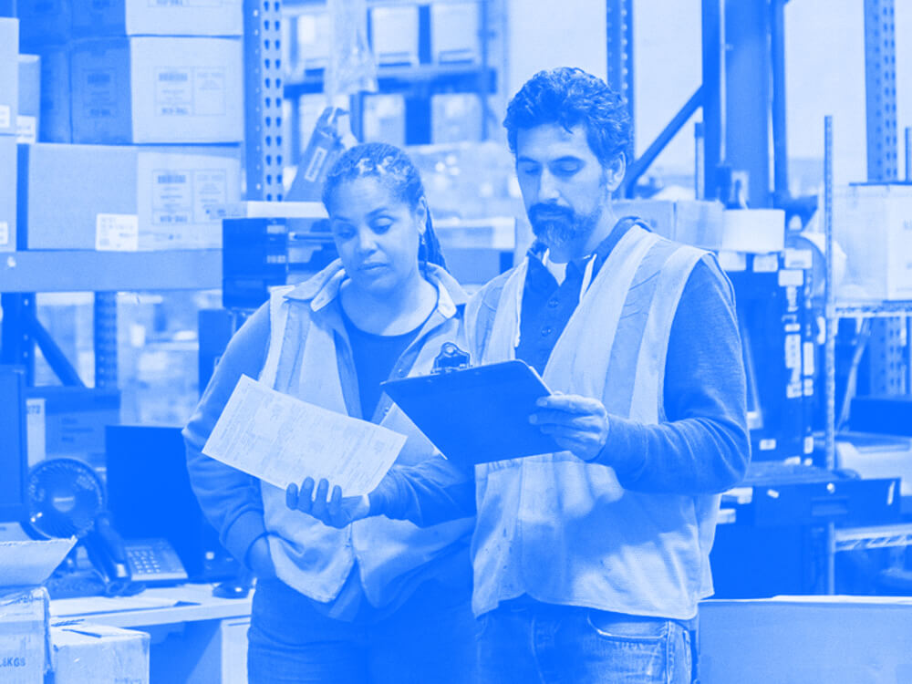 Two employees review a clipboard in a warehouse.