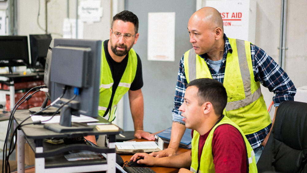 Three safety professionals huddle around a workstation.