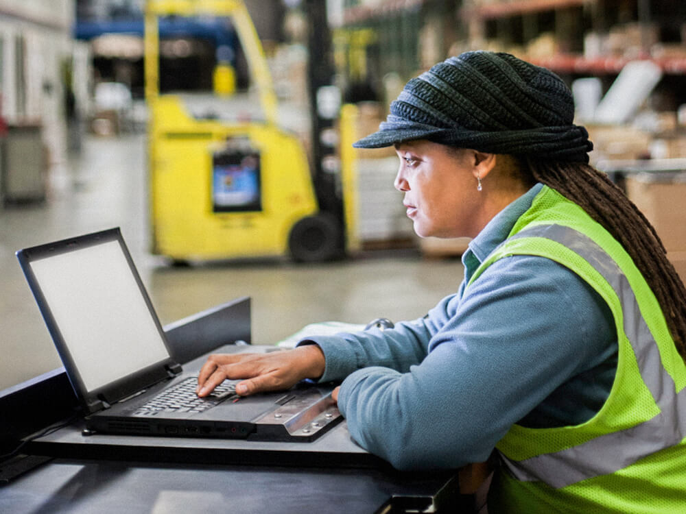 An employee works on a laptop in a warehouse.