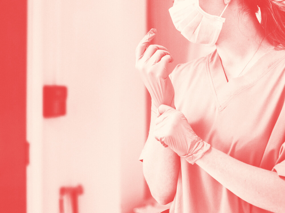 A perioperative nurse wears a mask and pulls on surgical gloves.