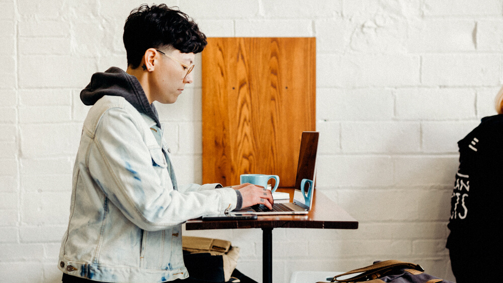 Computer technician wearing a jean jacket and hoodie works on a laptop.