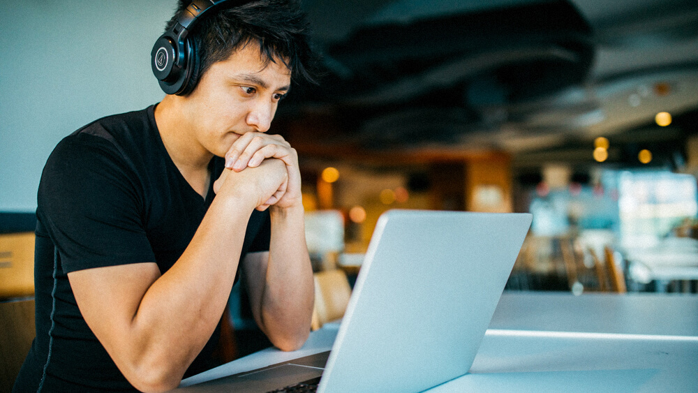 Cybersecurity analyst stares at computer screen with chin resting on folded hands.