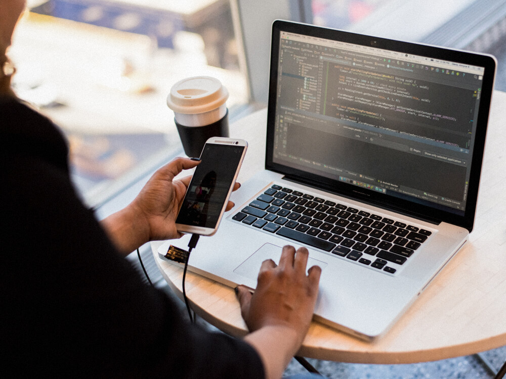 IT security specialist in an office holding a phone that is connected to a laptop. 