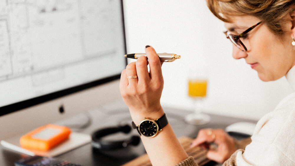 Financial securities expert holds a pen in one hand and enters numbers into a computer with other hand.