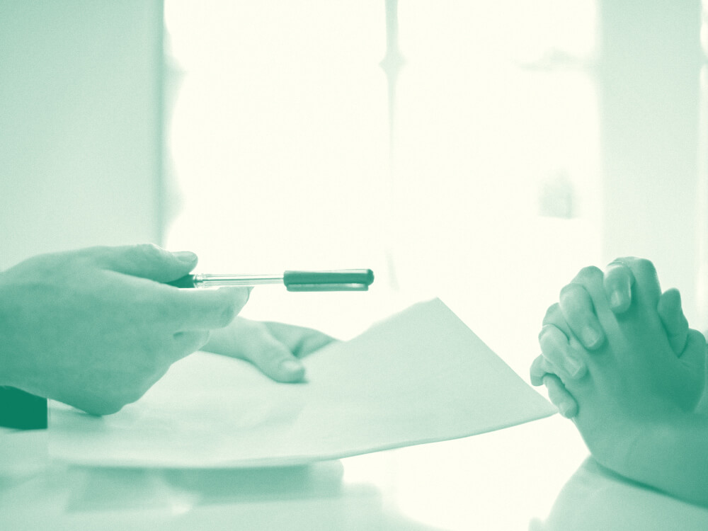 Hands holding out a pen and paper over a desk.