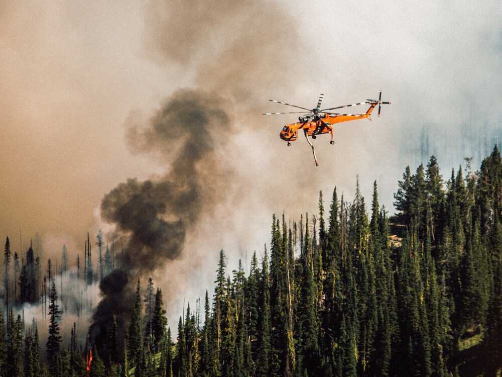 An orange emergency helicopter helps fight a forest fire.