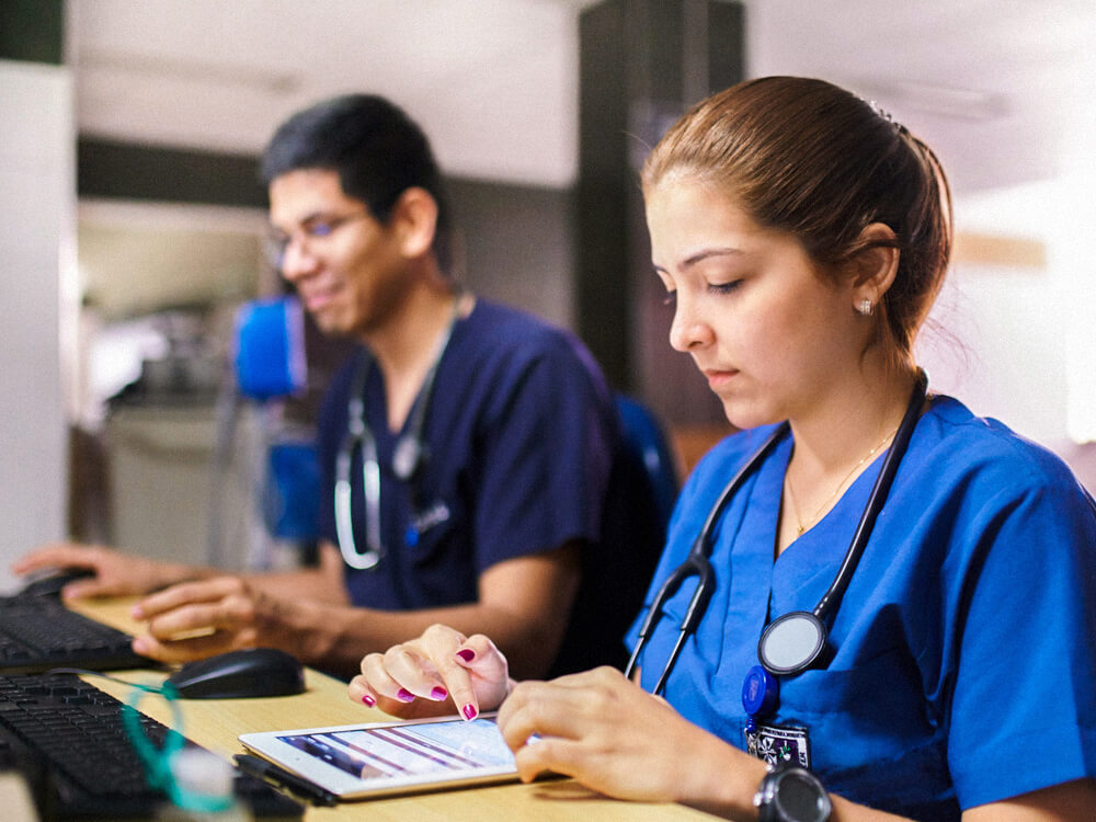 Two nursing students standing in front of a desk ledge. One of them is using a tablet.