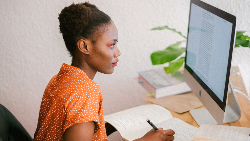 A student reads from a computer and takes notes.