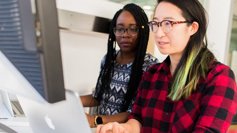 Two cloud security professionals work side by side together on computers.