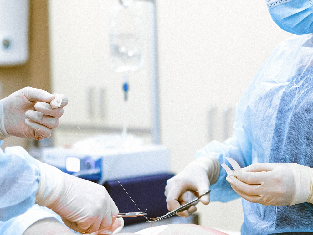 Two nurses assist in stitching up a patient.