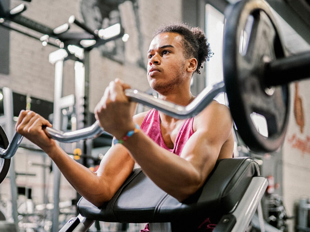 A person does seated bicep curls with a curl bar in a gym.