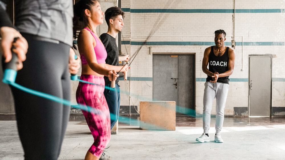 Personal trainer observes a group of people jumping rope in a gym.