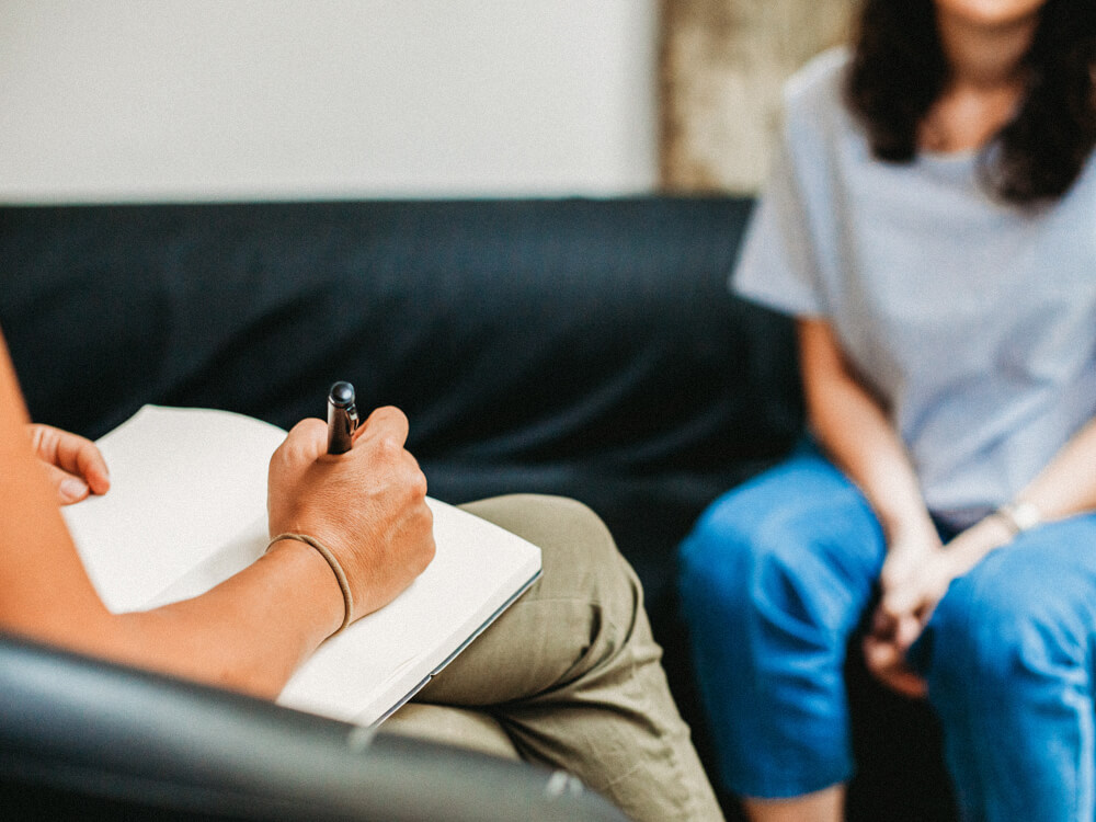 Counselor sits across from a client and takes notes during a session.