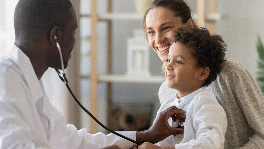 A physician assistant listens to the heart of a child patient with a stethoscope.