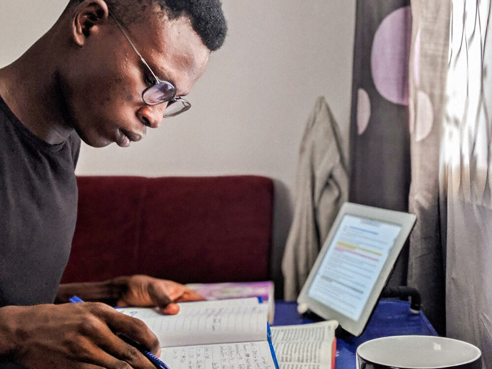 A student studies at a desk with notes, books, and a tablet.