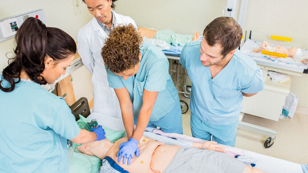 A group of student nurses practice CPR on a dummy while an instructor supervises.