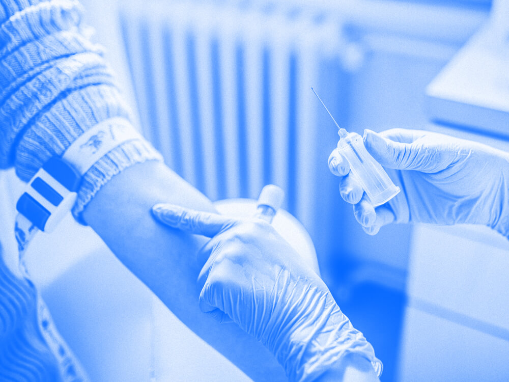 A phlebotomist marks a vein with one hand and holds a needle with the other hand.