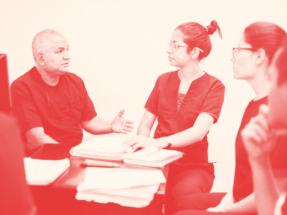 A nurse educator works with a group of nurses around their desk.