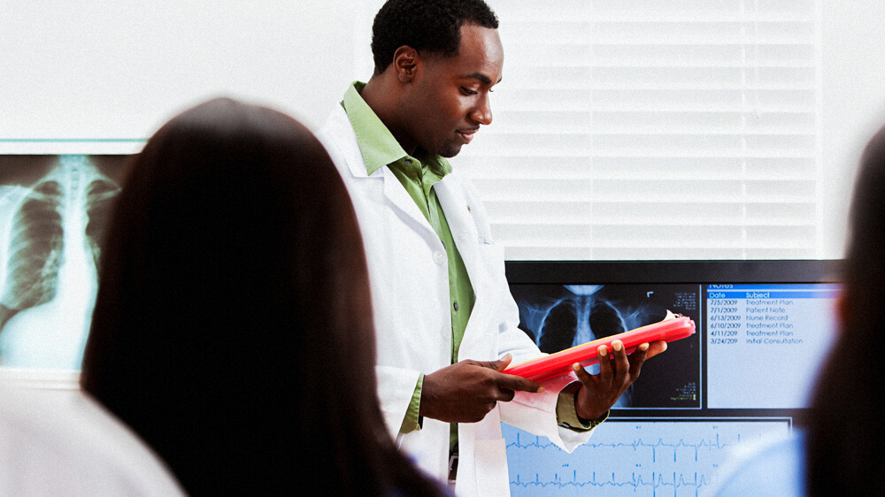 A nurse educator stands in front of seated nurses and reviews an x-ray.