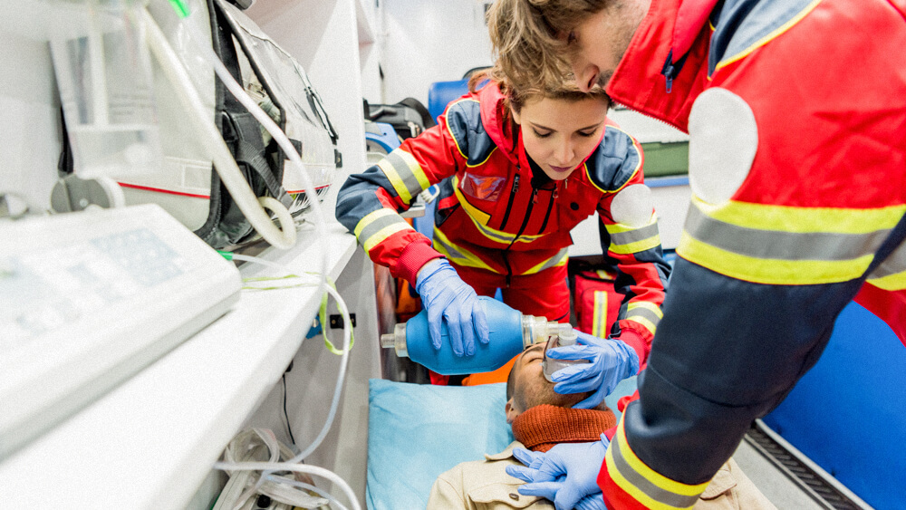 Two EMTs hook a patient up to oxygen in an ambulance.