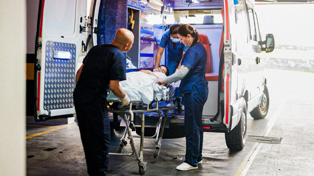 Three paramedics load a patient on a stretcher into an ambulance.