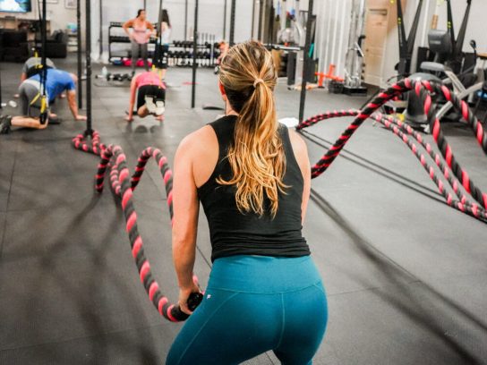 An athlete performs a double wave exercise using battle ropes in a gym.