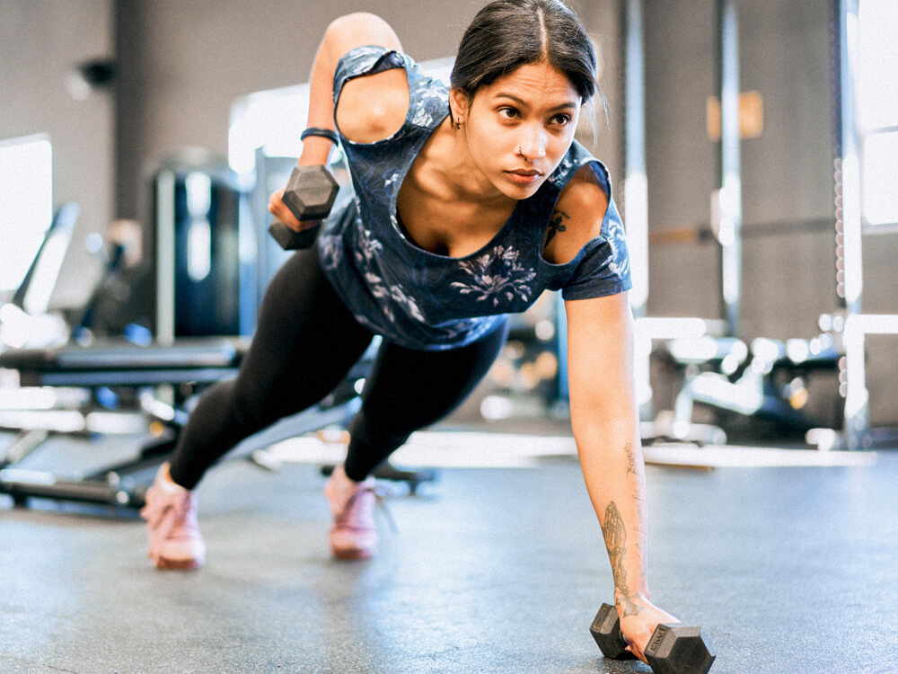 Person performs plank side rows with dumbbells in a gym.