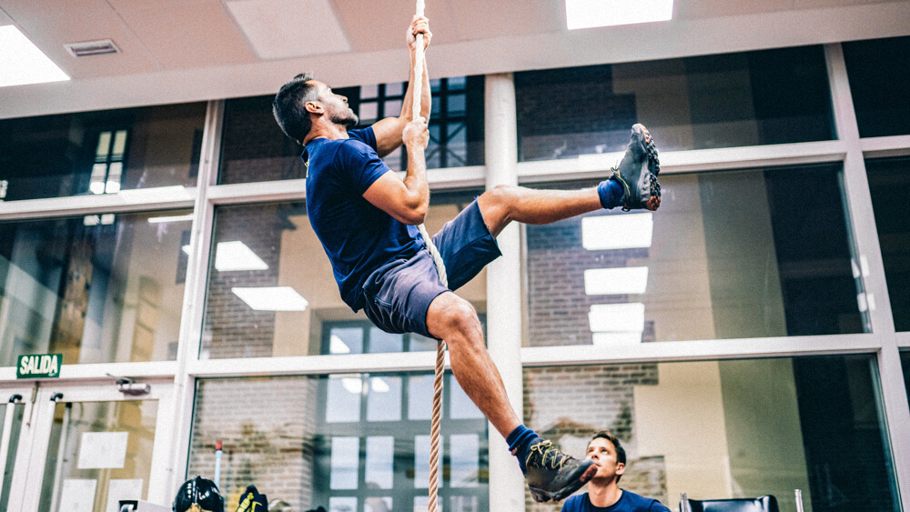 Person climbs up a rope using only their arms in a gym.