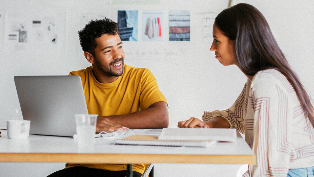 Two employees work together at a table in a meeting room.