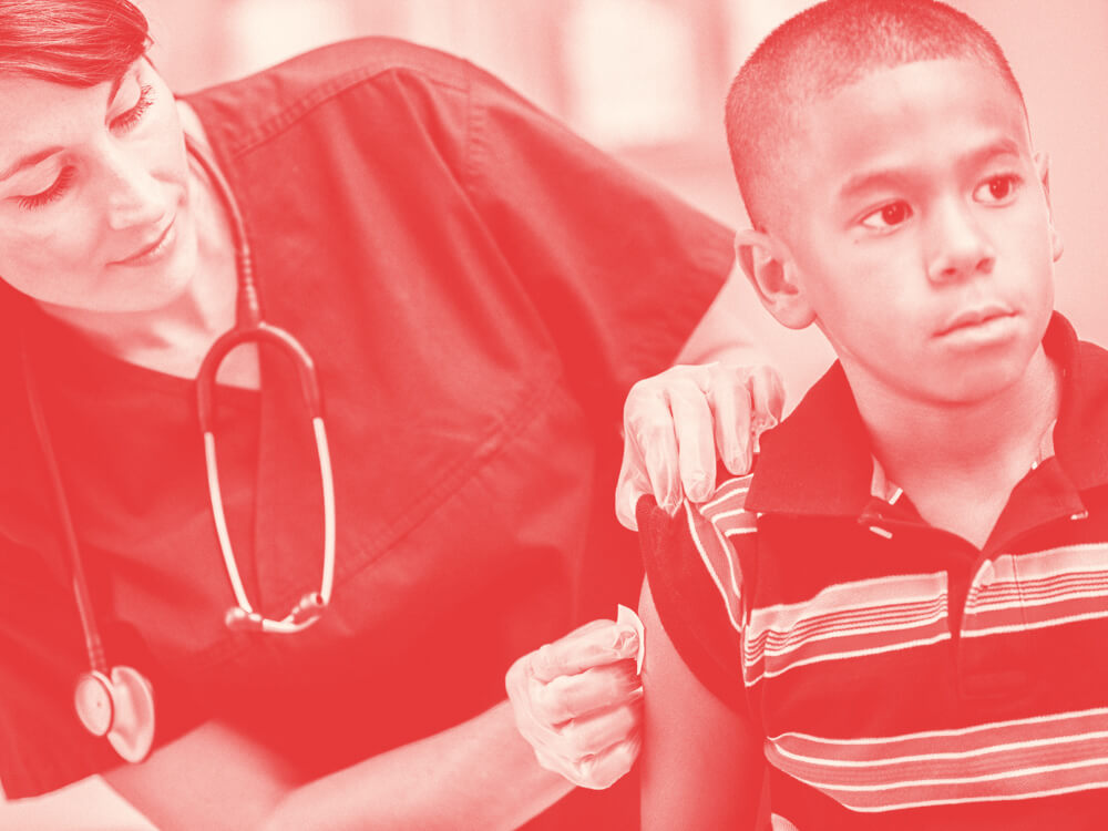 A pediatric nurse cleans a spot on a child’s upper arm.