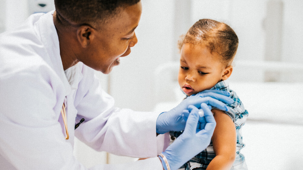 A pediatric nurse gives a child a shot in the upper arm.