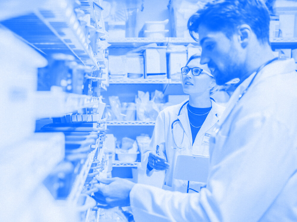 Two pharmacy technicians in front of shelves of medications.