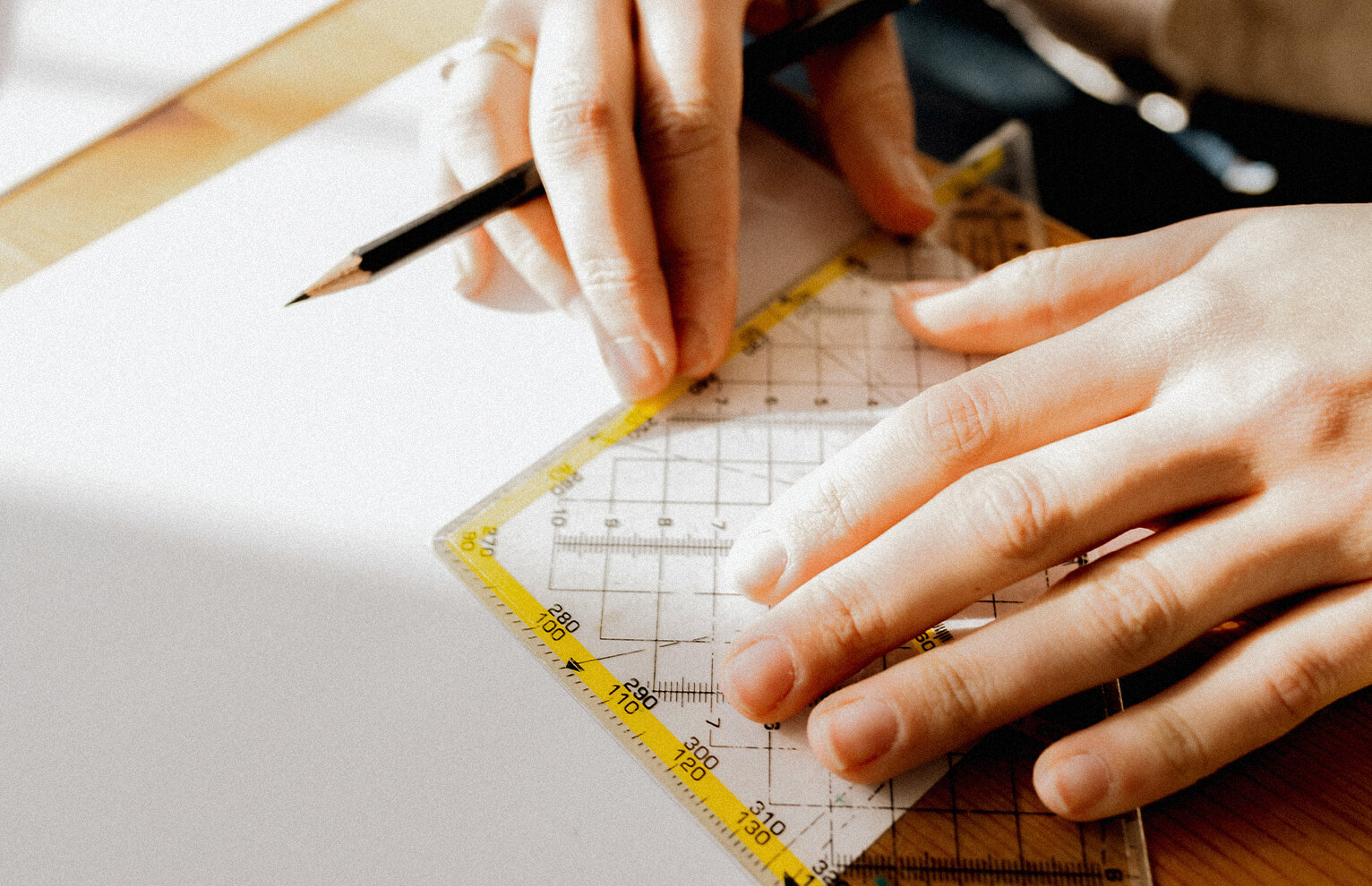 Hands with protractor and pencil on blank paper. Close-up.