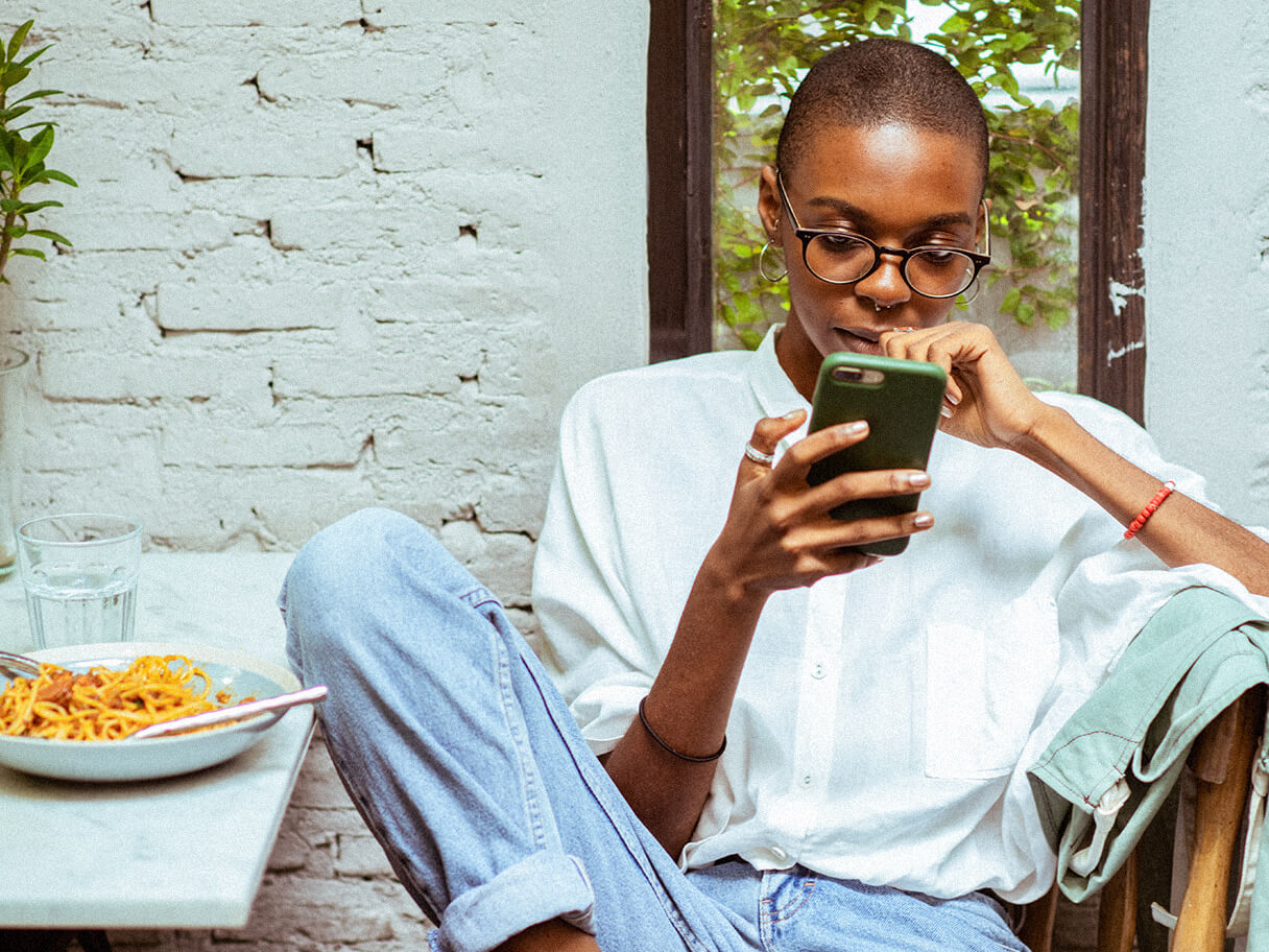 A student studies on their phone with their leg propped up against a dining table.