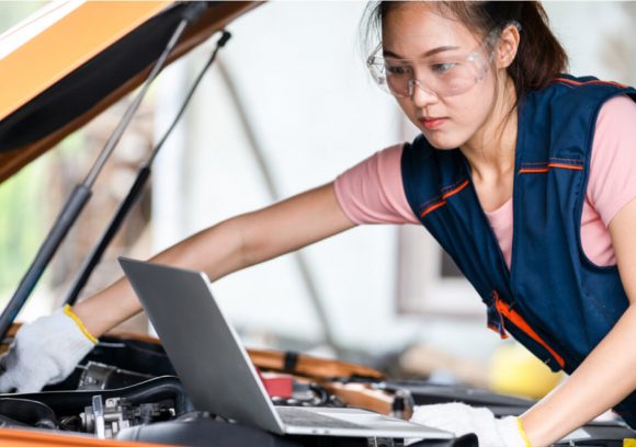 Automotive technician works on an engine while looking at a computer.